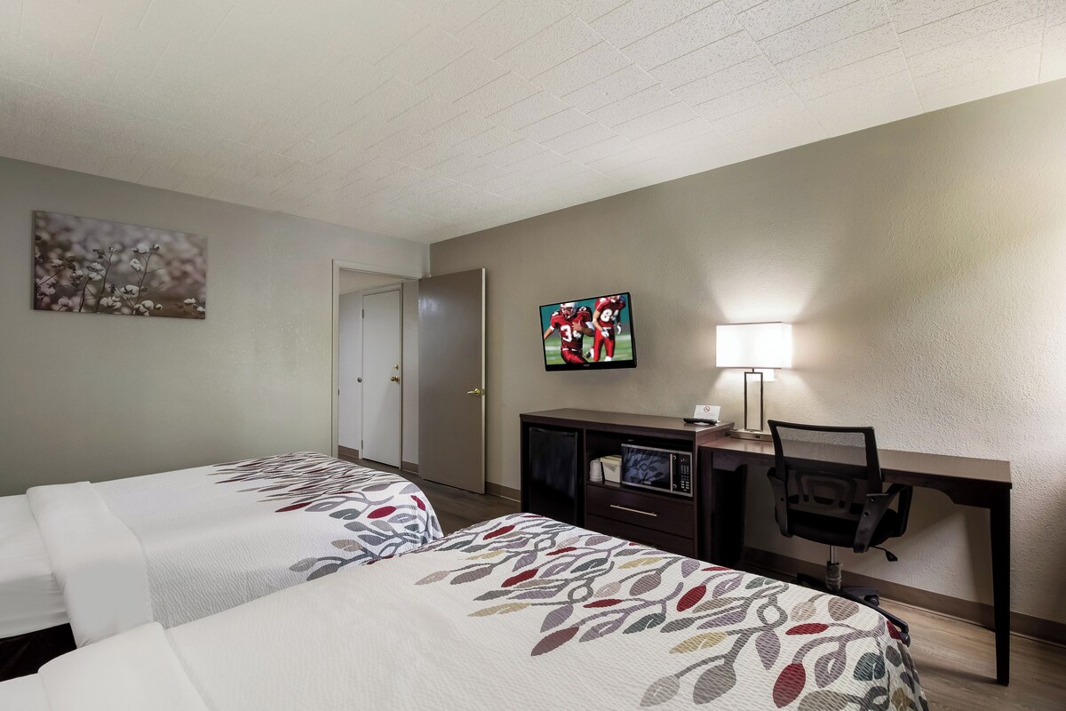 Une chambre d’hôtel avec deux lits, un bureau avec un ordinateur, une télévision et une lampe.