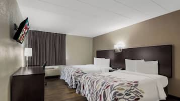 A hotel room with two beds, a flat-screen TV mounted on the wall, a desk, and a window with curtains.
