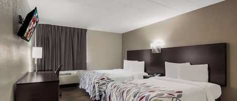 A hotel room with two beds, a flat-screen TV mounted on the wall, a desk, and a window with curtains.