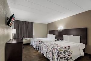 A hotel room with two beds, a flat-screen TV mounted on the wall, a desk, and a window with curtains.