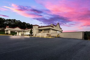 A modern building with a parking lot, a covered entrance, and a landscaped area with trees. - Red Roof Inn New Stanton (New Stanton)