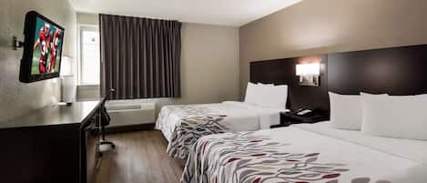 Ein Hotelzimmer mit Bett, Nachttisch, Lampe und einem an der Wand befestigten Fernseher.