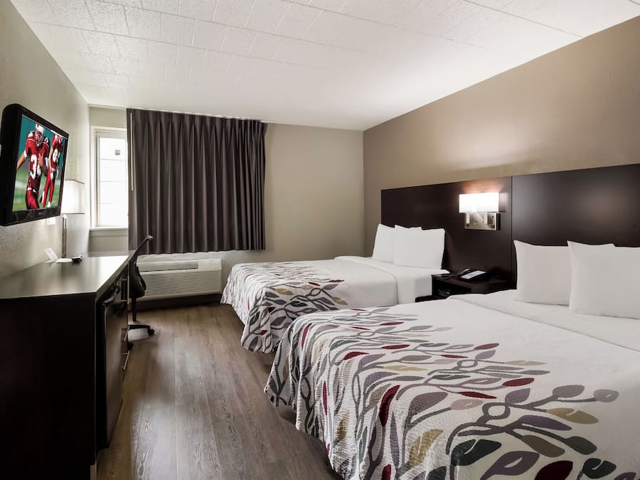 A hotel room with a bed, bedside table, lamp, and a TV mounted on the wall.