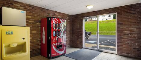 A vending machine with a Coca-Cola logo, a yellow ice dispenser, and a glass door leading outside.