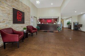 Un espace d’accueil avec une enseigne Red Roof Inn, un comptoir de réception et deux chaises rouges.