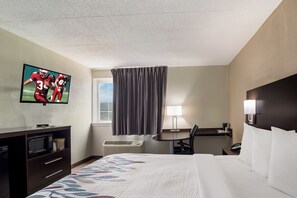 Une chambre d’hôtel équipée d’un lit, d’un bureau, d’une télévision, d’un four à micro-ondes et d’une fenêtre avec des rideaux.
