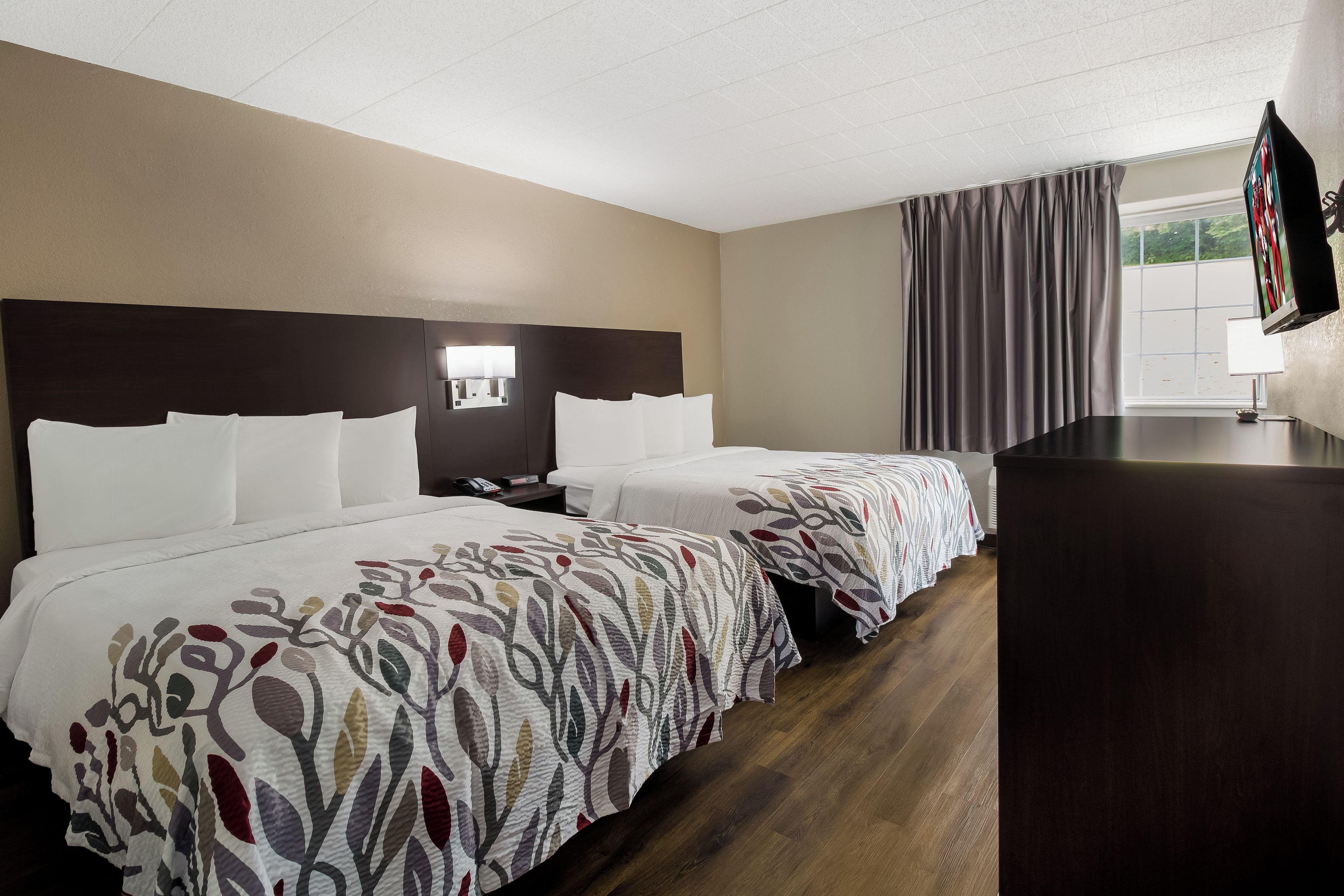 A hotel room with two beds, a desk, a TV, and a window with curtains.
