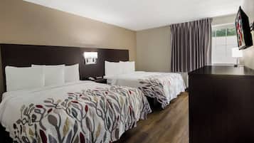 A hotel room with two beds, a desk, a TV, and a window with curtains.