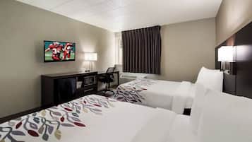 A hotel room with two beds, a flat-screen TV mounted on the wall, a desk with a chair, a lamp, and a window with curtains.