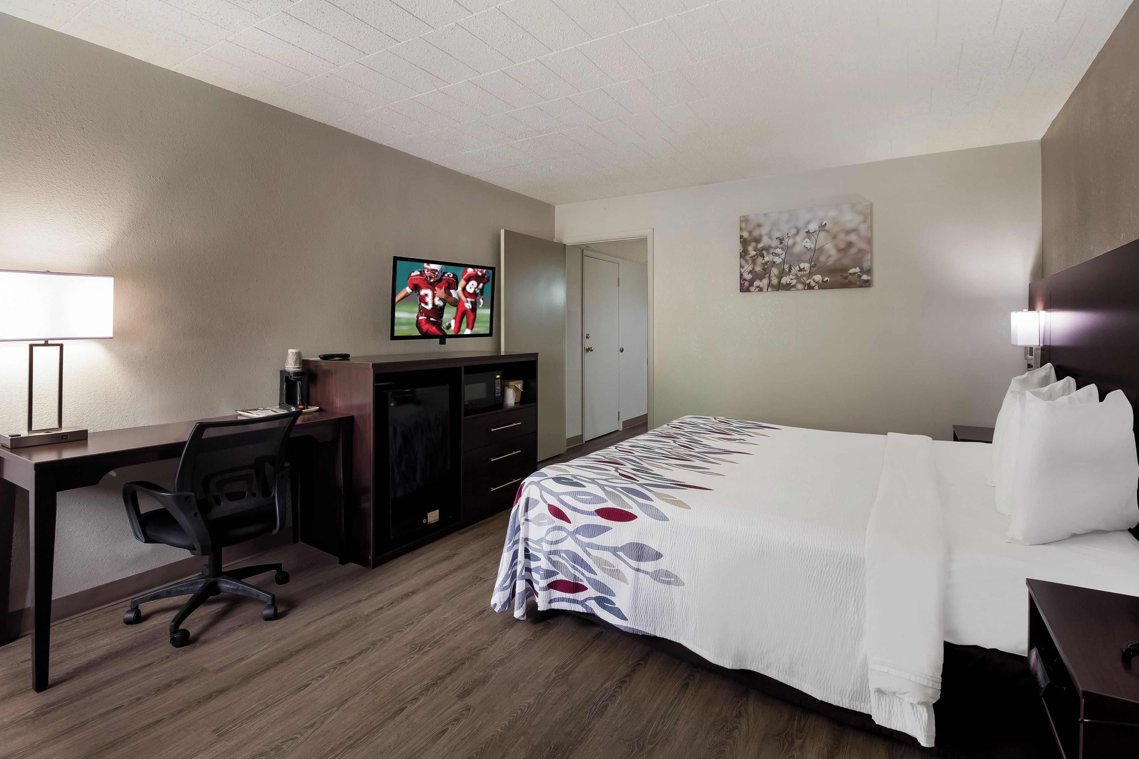 A hotel room with a bed, desk, chair, television, and artwork on the walls.