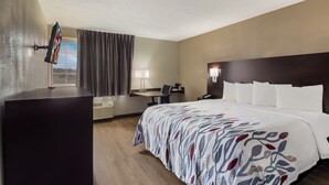 Habitación de hotel con una cama grande, un escritorio con una computadora portátil, un televisor montado en la pared y una ventana con cortinas.