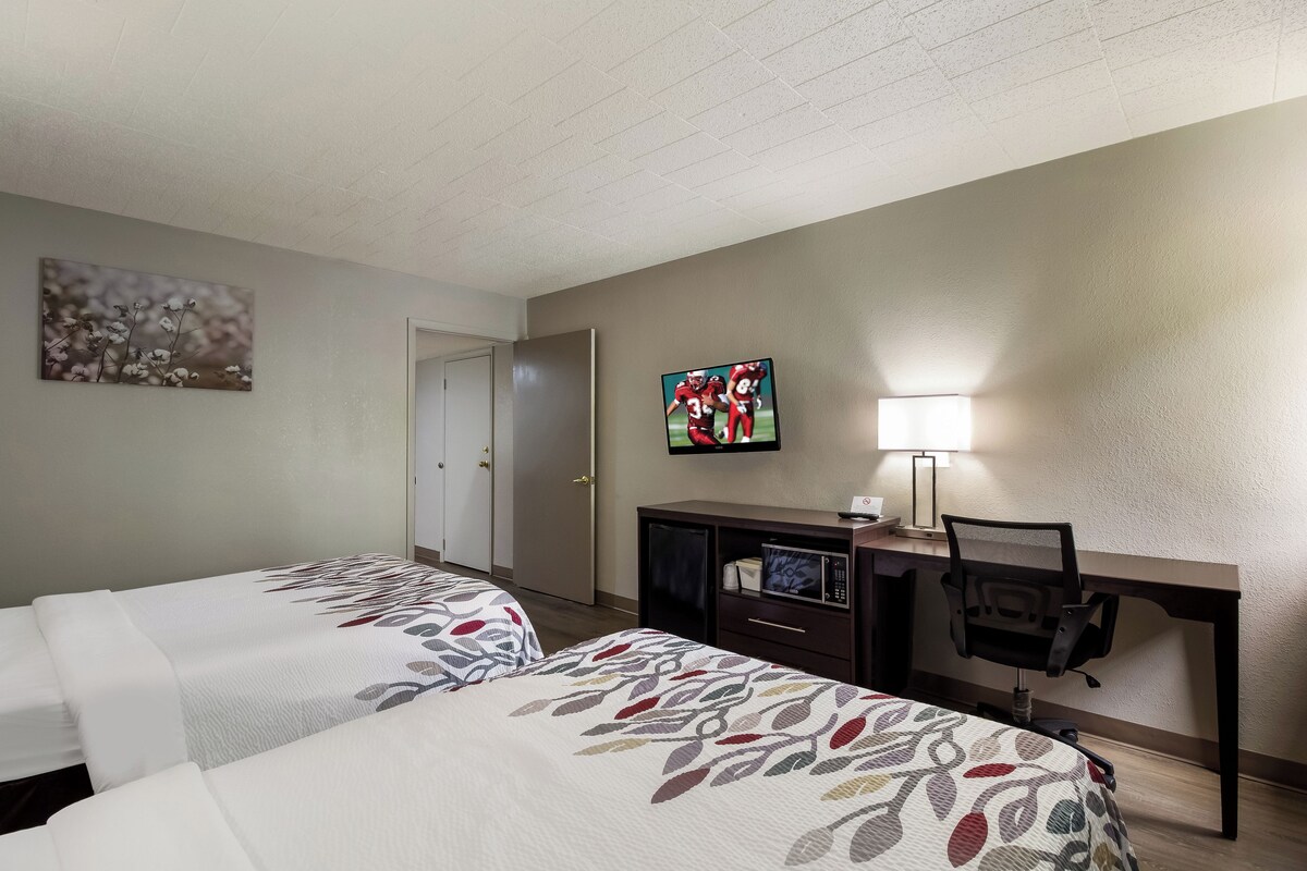 Une chambre d’hôtel avec deux lits, un bureau avec un ordinateur, une télévision et une lampe.