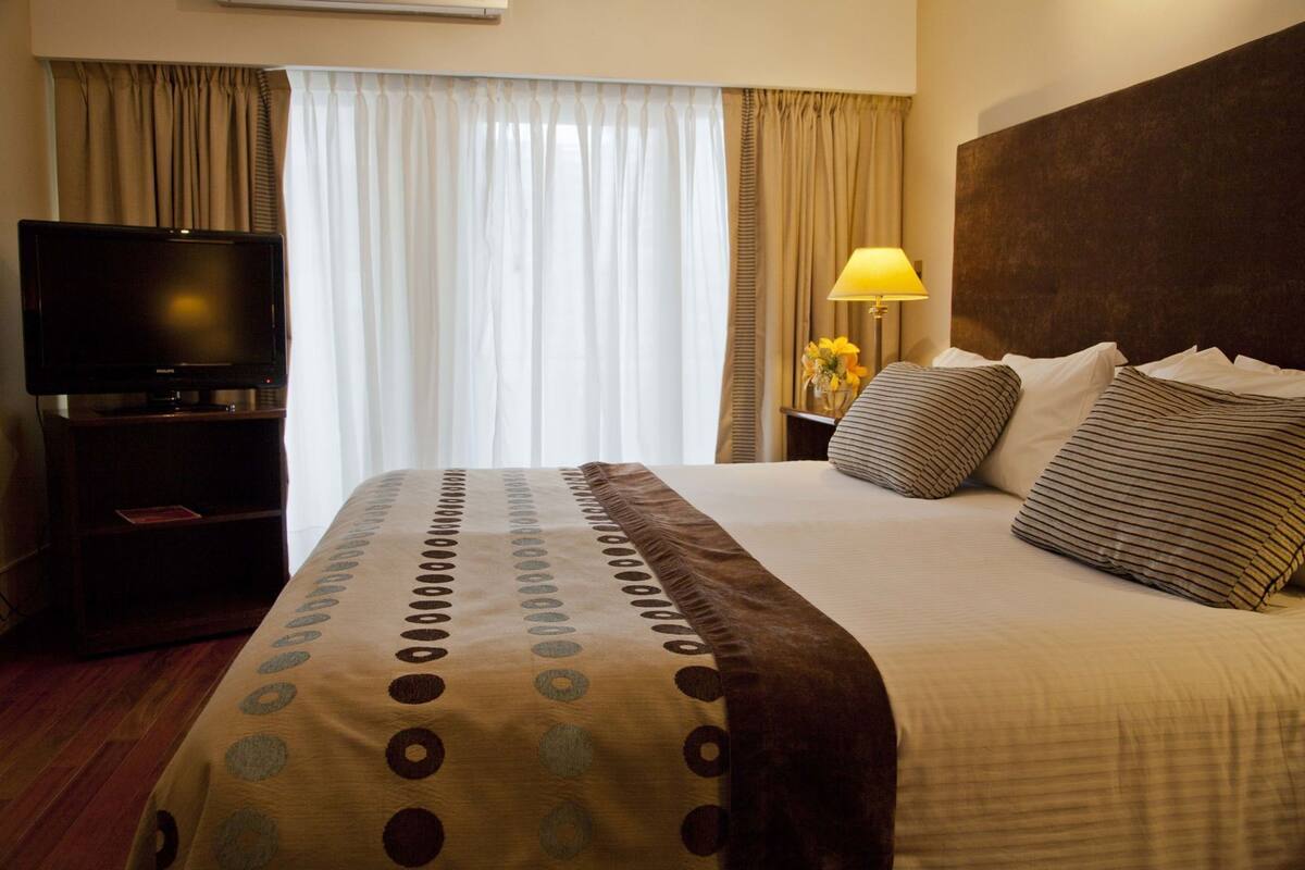 A hotel room with a bed, a television on a stand, a lamp, and curtains.