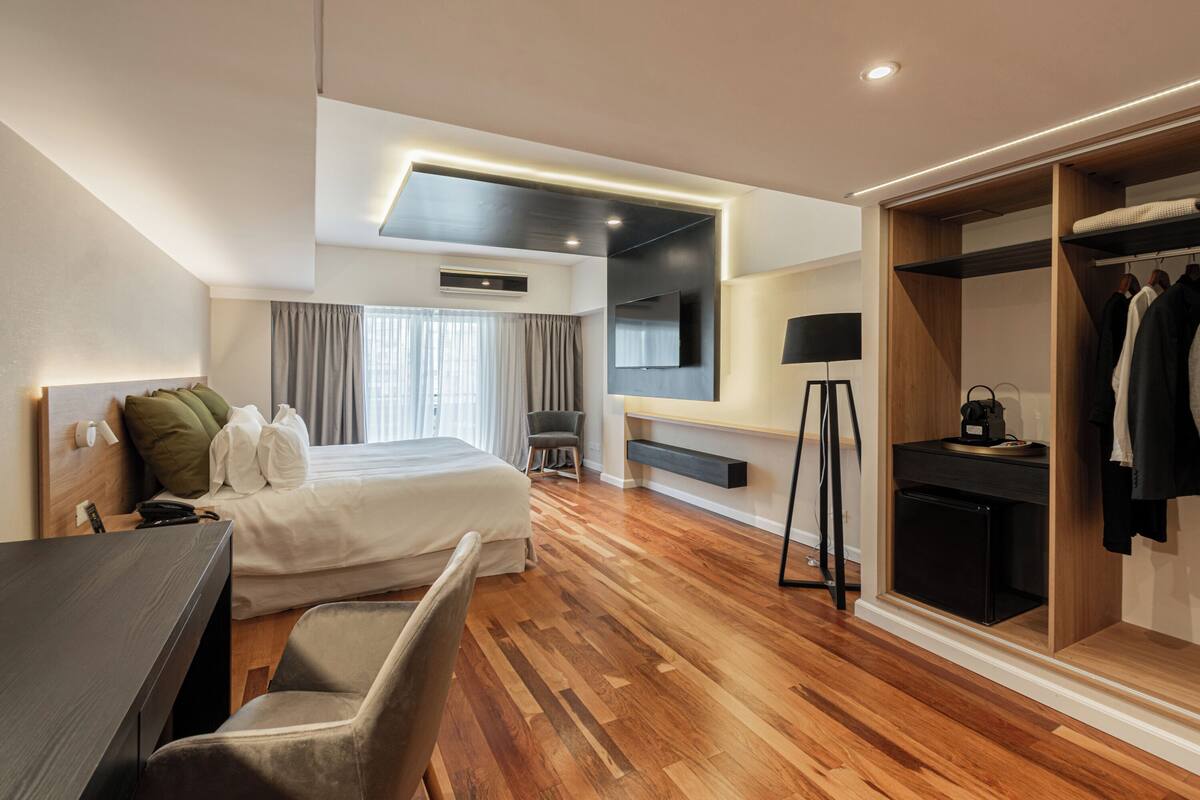A modern hotel room with a bed, desk, chair, wardrobe, and a TV mounted on the wall.