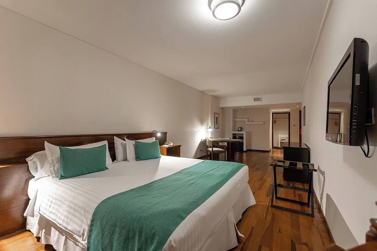 A hotel room with a large bed, a desk, and a television mounted on the wall.