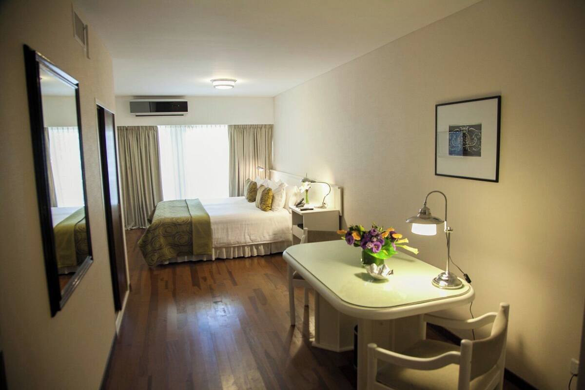 A hotel room with a bed, bedside table, desk, chair, and a desk lamp.