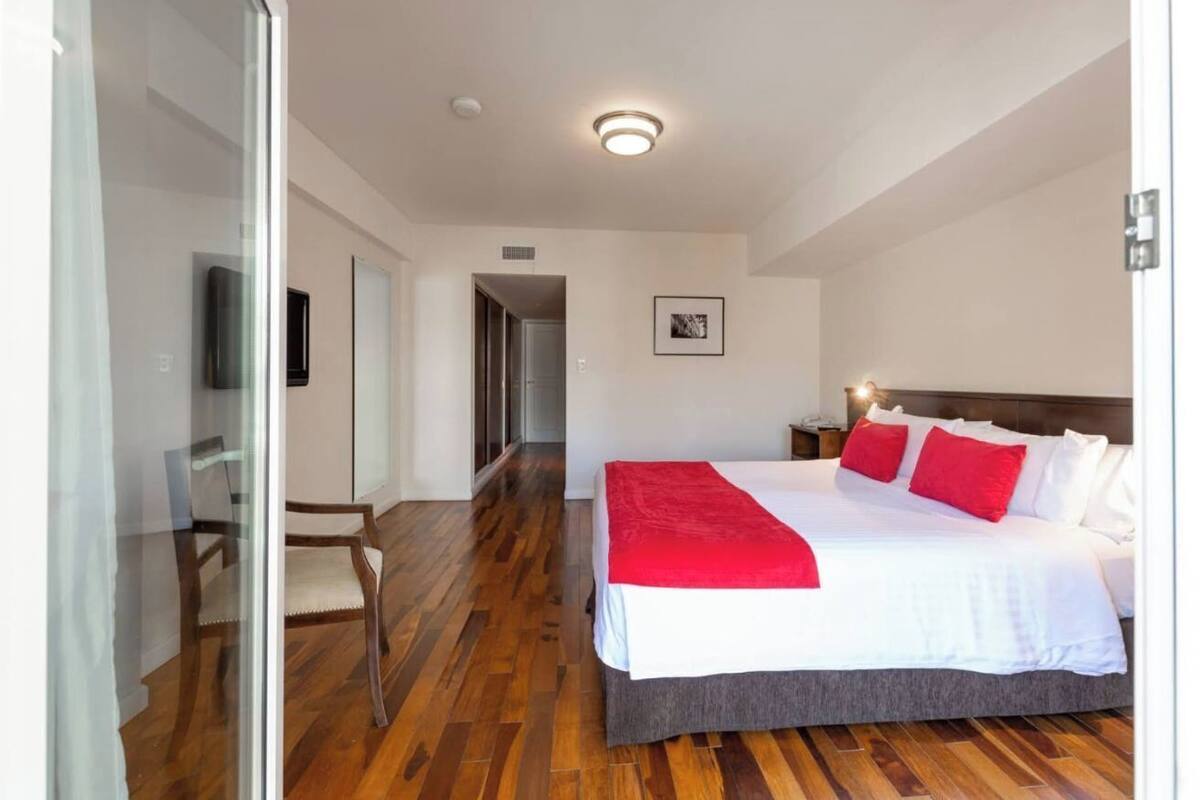 A modern hotel room with a large bed, a glass door leading to a balcony, and a wooden floor.