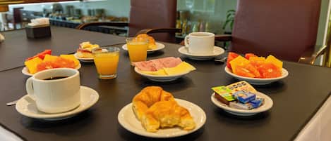 Un desayuno con cruasanes, rodajas de naranja, café y jugo sobre una mesa.