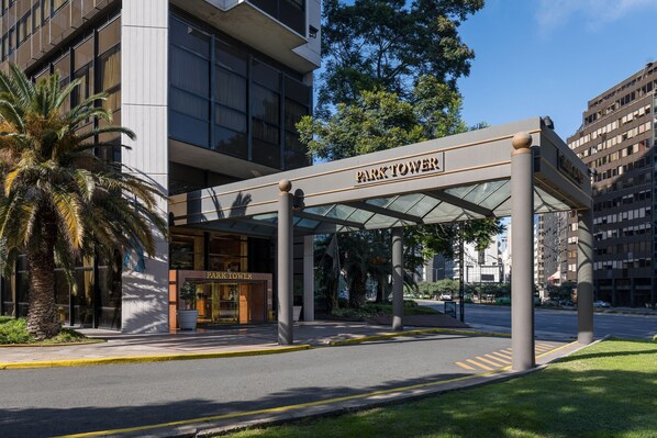 A modern hotel entrance with a covered walkway, palm trees, and a clear sky.