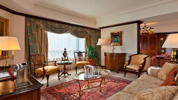 Una habitación tradicional con sofá, sillones, una mesita de centro, chimenea y un ventanal con cortinas.