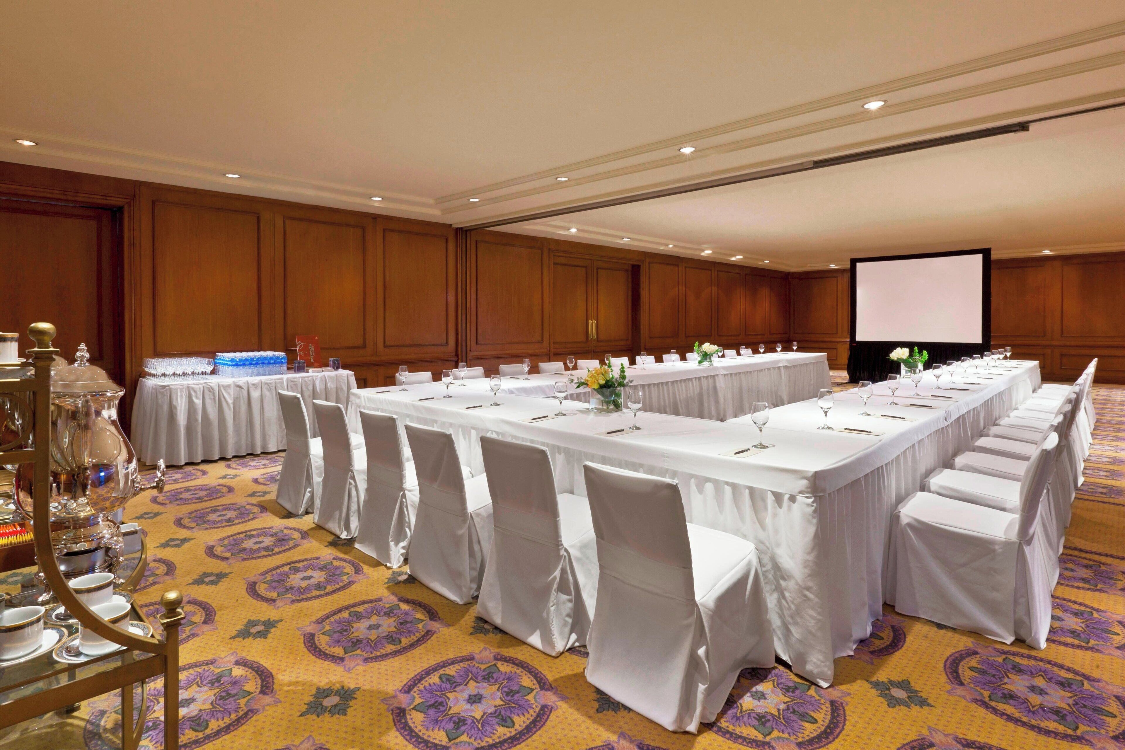 A conference room with a long table, white chairs, and a projector screen.