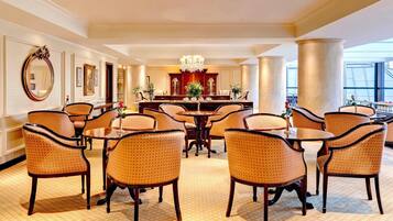 Un comedor amplio con mesas y sillas redondas, un candelabro central y ventanas grandes.