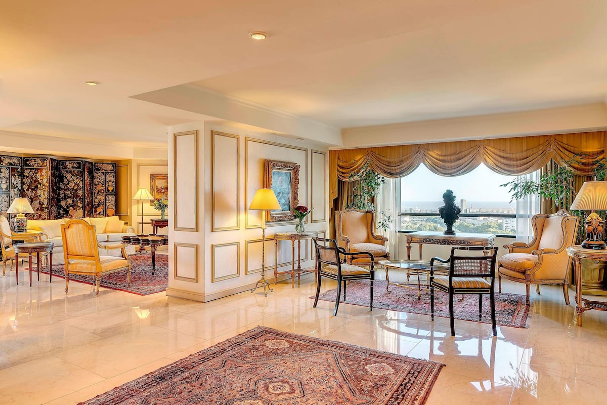 A spacious living room with a large window, elegant furniture, and a decorative rug.