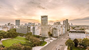 A cityscape with modern high-rise buildings, a central park, and a wide road with vehicles.