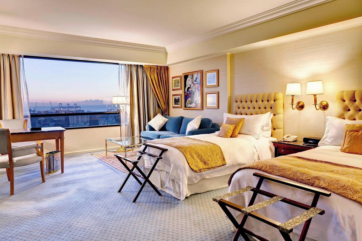 A hotel room with a large window, a bed, a desk, and a chair.