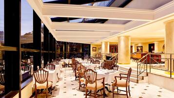 A spacious dining area with multiple tables and chairs, large windows, and a view of the cityscape.