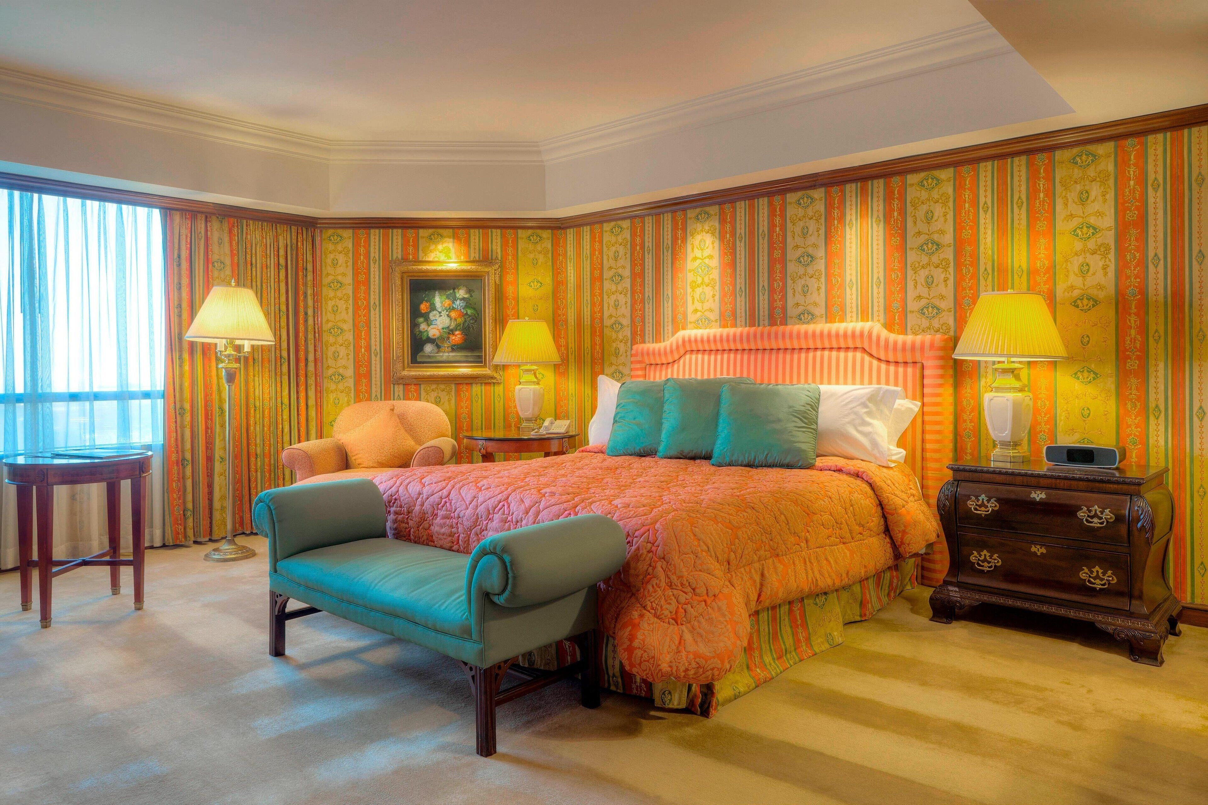 A bedroom with a large bed, two bedside tables with lamps, a chair, and a small table.