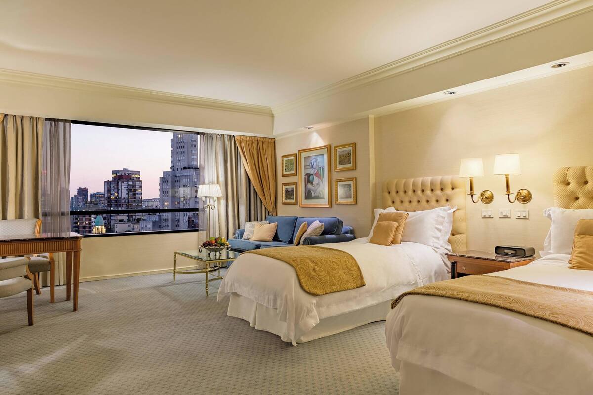 A hotel room with a city view, a bed, a sofa, a desk, and a chair.