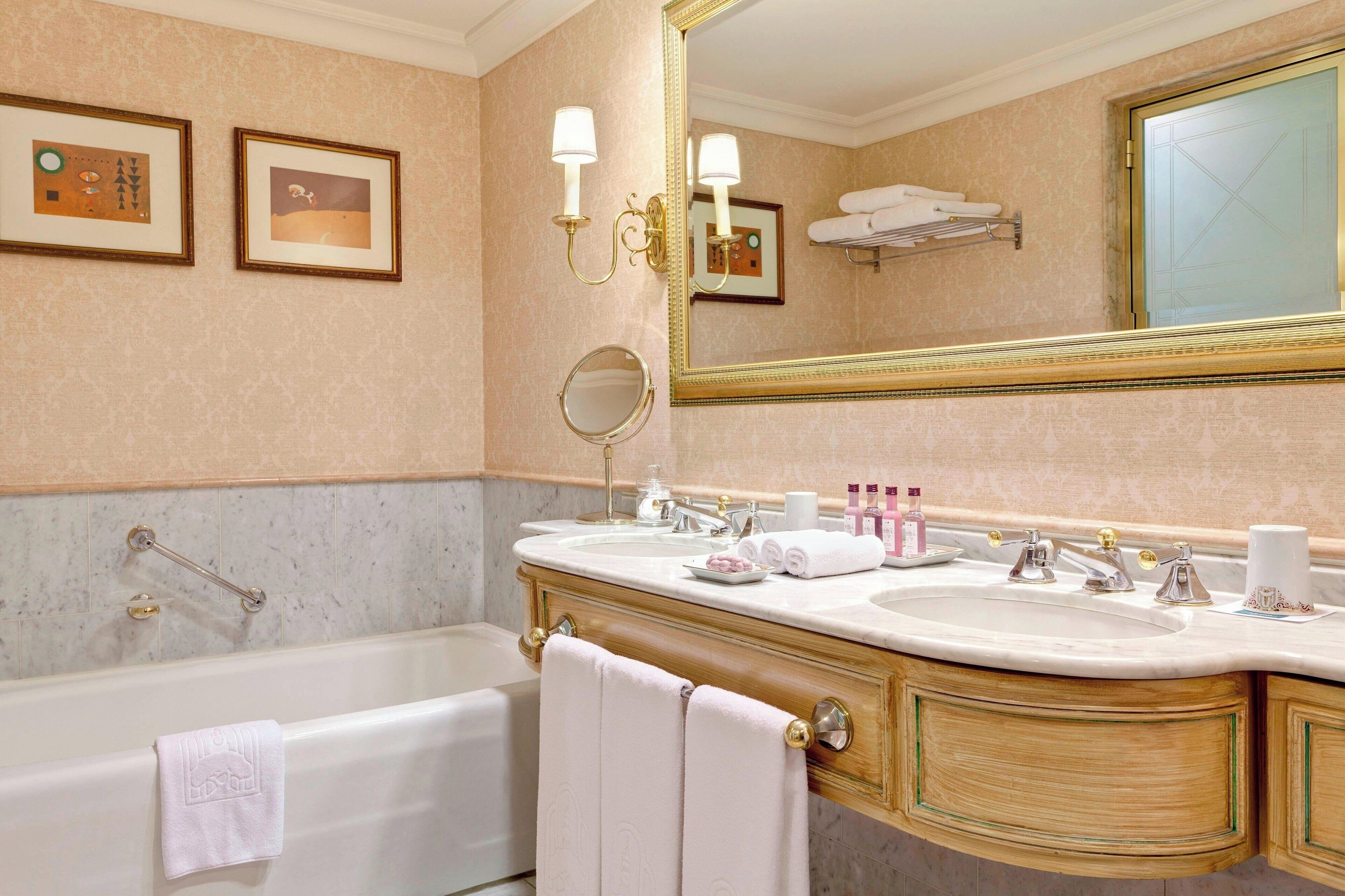 A bathroom with a double sink vanity, a bathtub, a large mirror, framed artwork on the wall, and a towel rack.