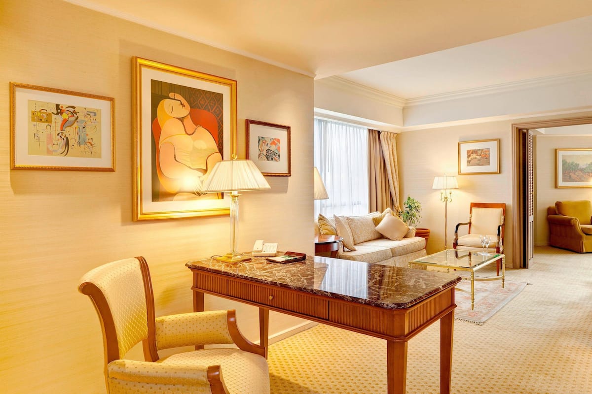 A hotel room with a marble coffee table, a sofa, a chair, and artwork on the walls.