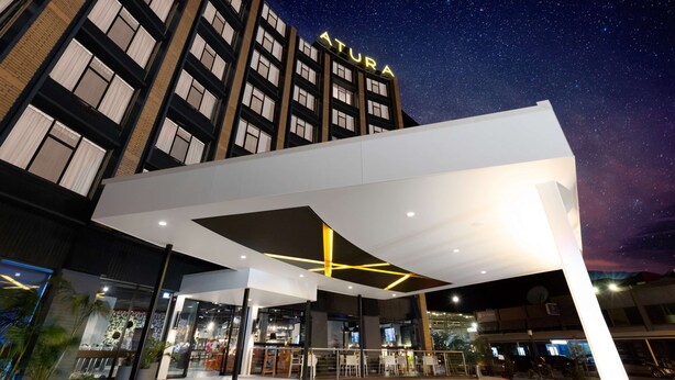 A modern hotel with a prominent 'ATURA' sign, a covered outdoor area with seating, and a view of the night sky. - Atura Albury (Albury)