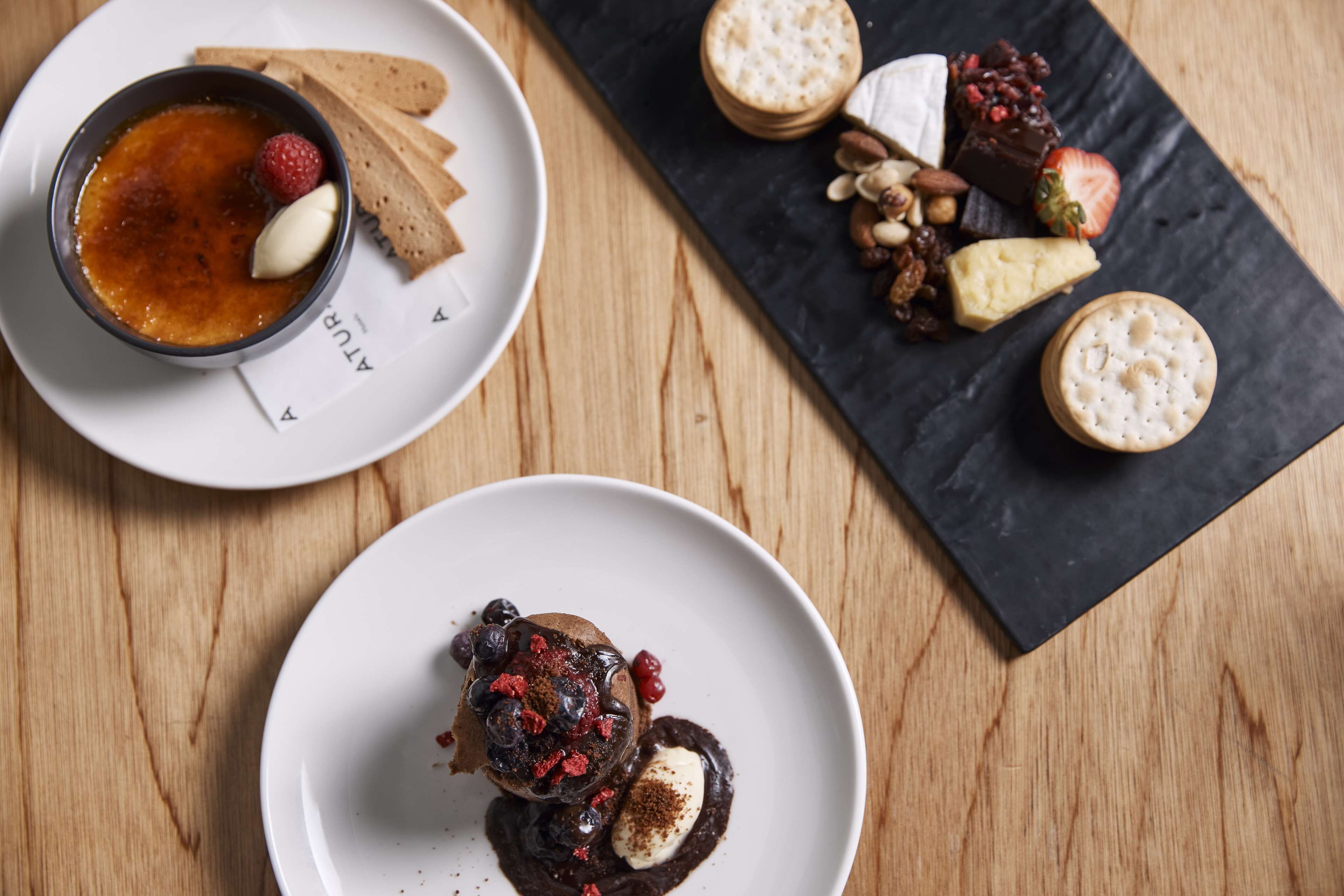 A dessert plate with chocolate mousse and berries, a bowl of crème brûlée, and a selection of cheeses and nuts on a slate board.
