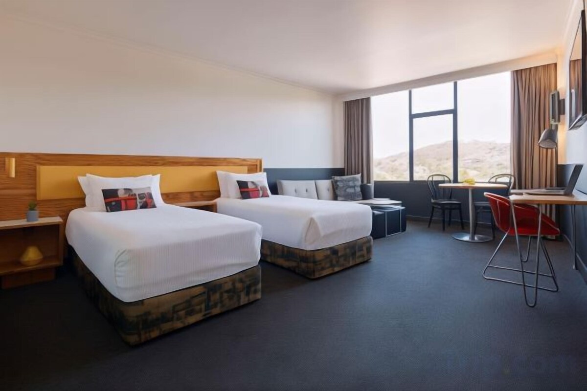 A hotel room with two beds, a desk, and a view of the desert.