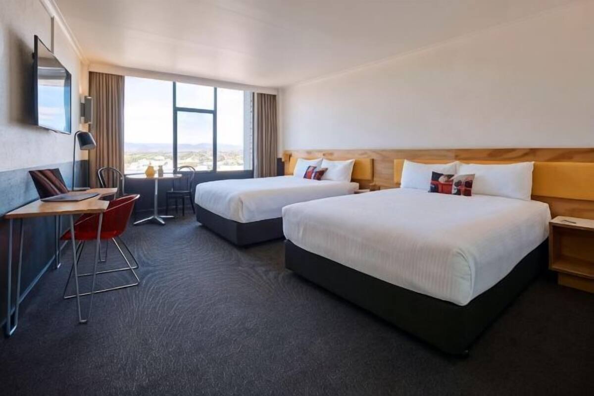 A hotel room with two beds, a desk, a chair, a TV, and a window with a view.
