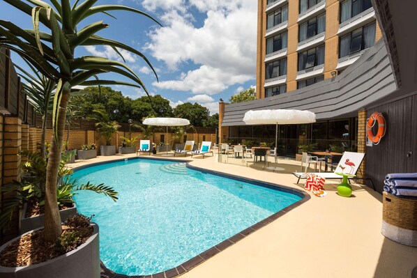 Relax by the pool surrounded by lounge chairs and umbrellas, with a lifebuoy nearby for added safety.