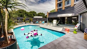 A swimming pool with a decorative cow float, lounge chairs, and a building in the background. - Atura Albury (Albury)