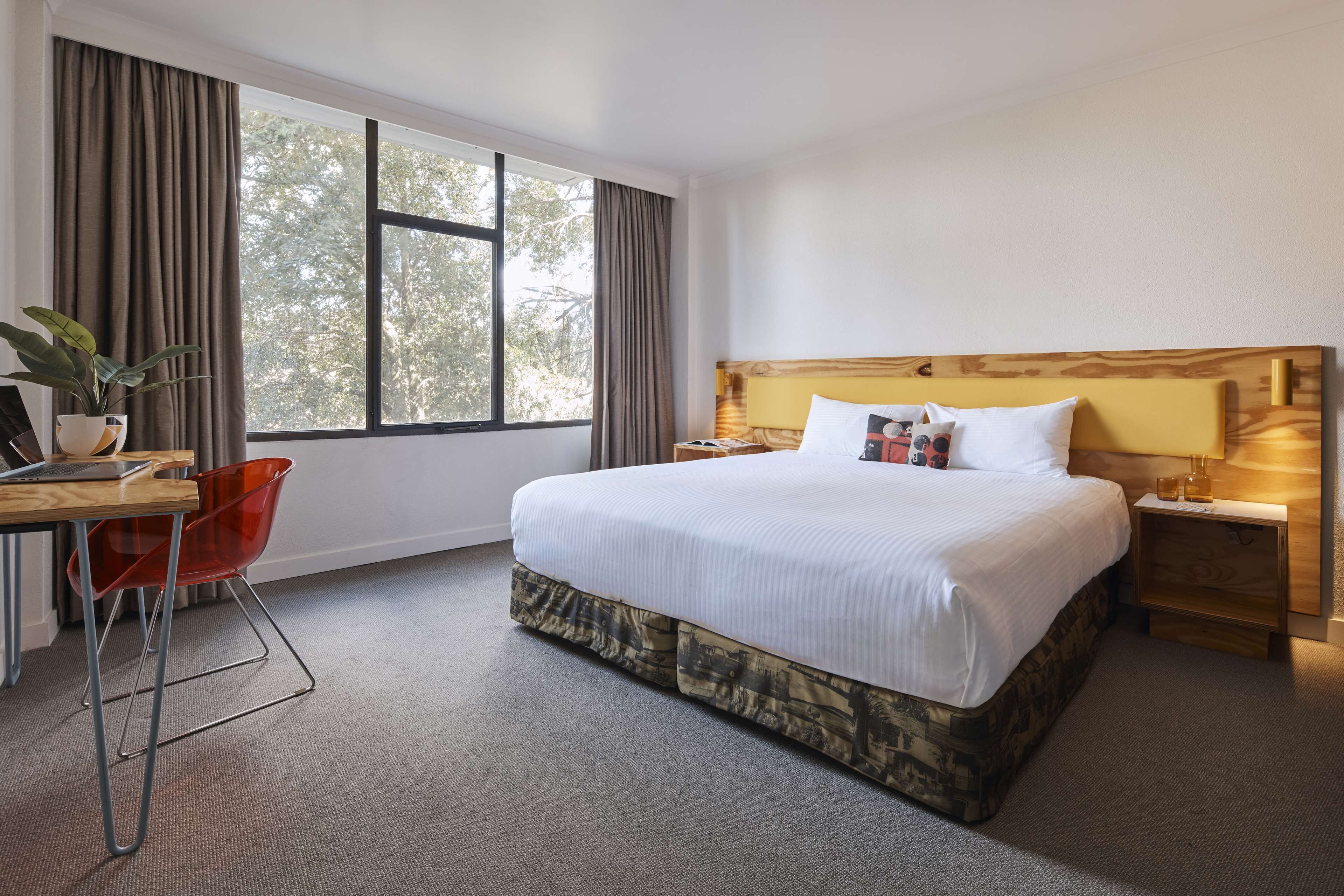 Habitación de hotel con una cama grande, un escritorio con silla, una mesita de noche y una ventana con cortinas.