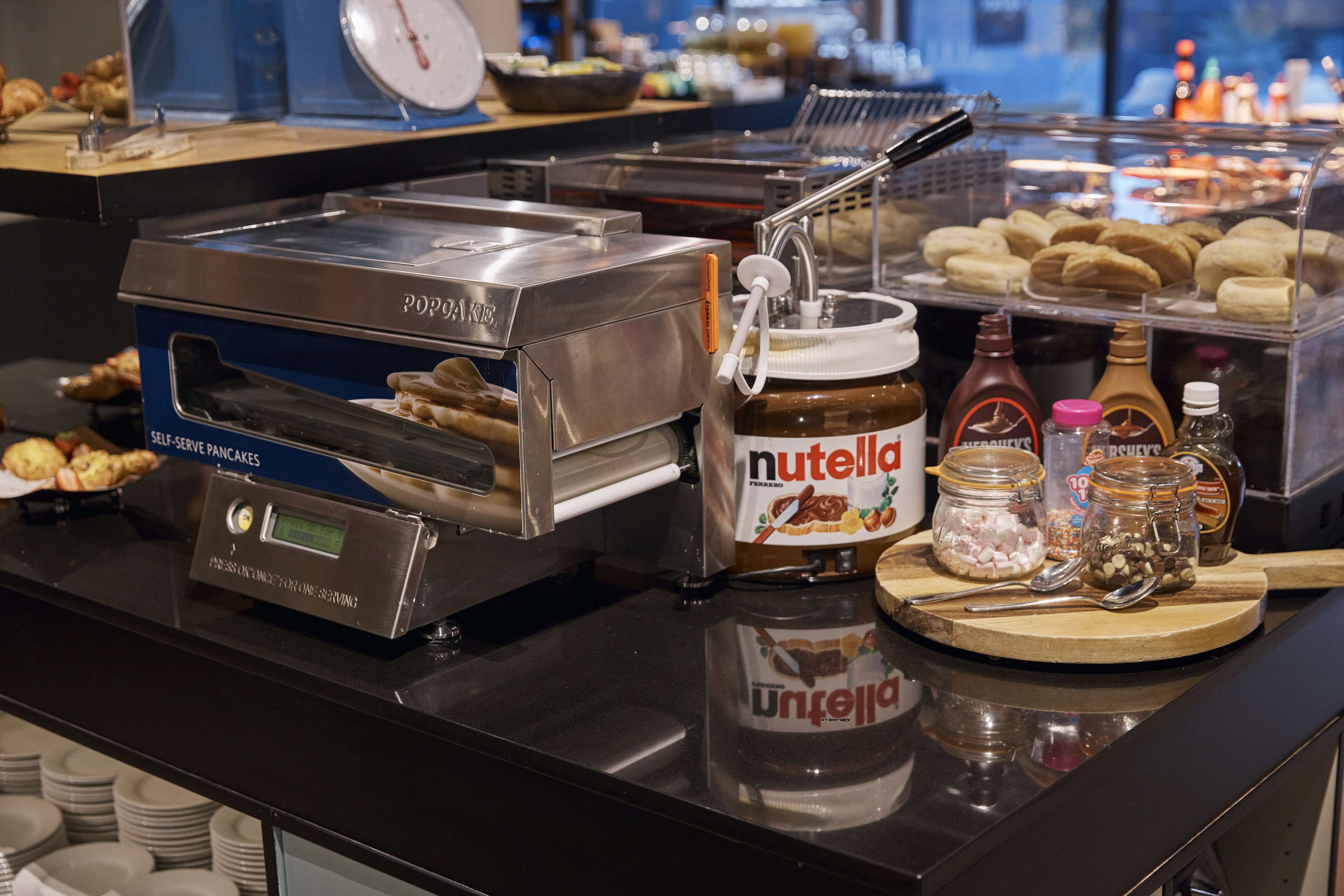 Een pannenkenstation met zelfbediening, inclusief een digitaal scherm, een Nutella-dispenser en diverse toppings.