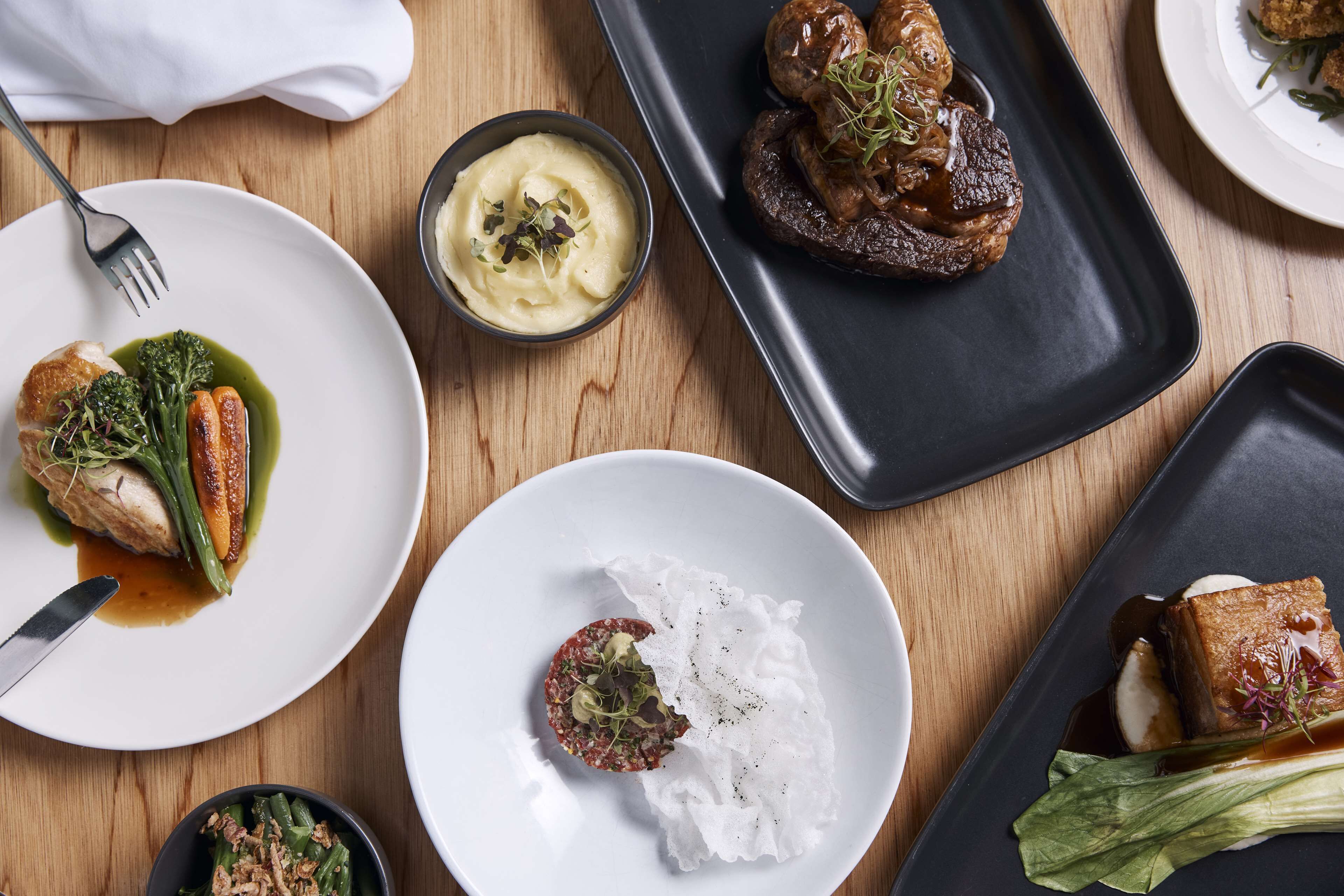 A variety of dishes on different plates, including a steak, a fish dish, and a dessert.