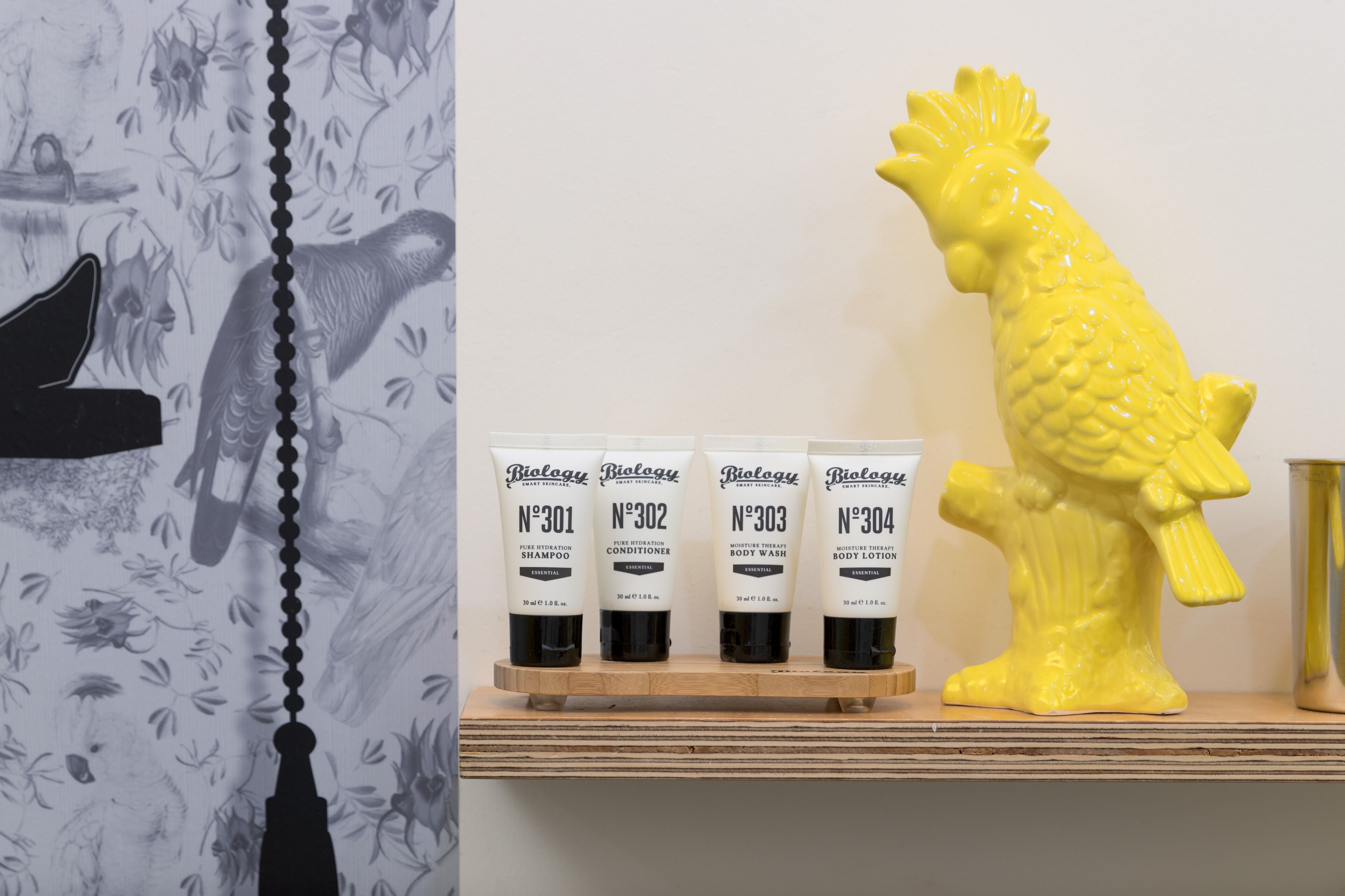 Uma prateleira com quatro frascos de produtos de cuidados para o corpo Biolgy e um peixe de cerâmica amarelo.