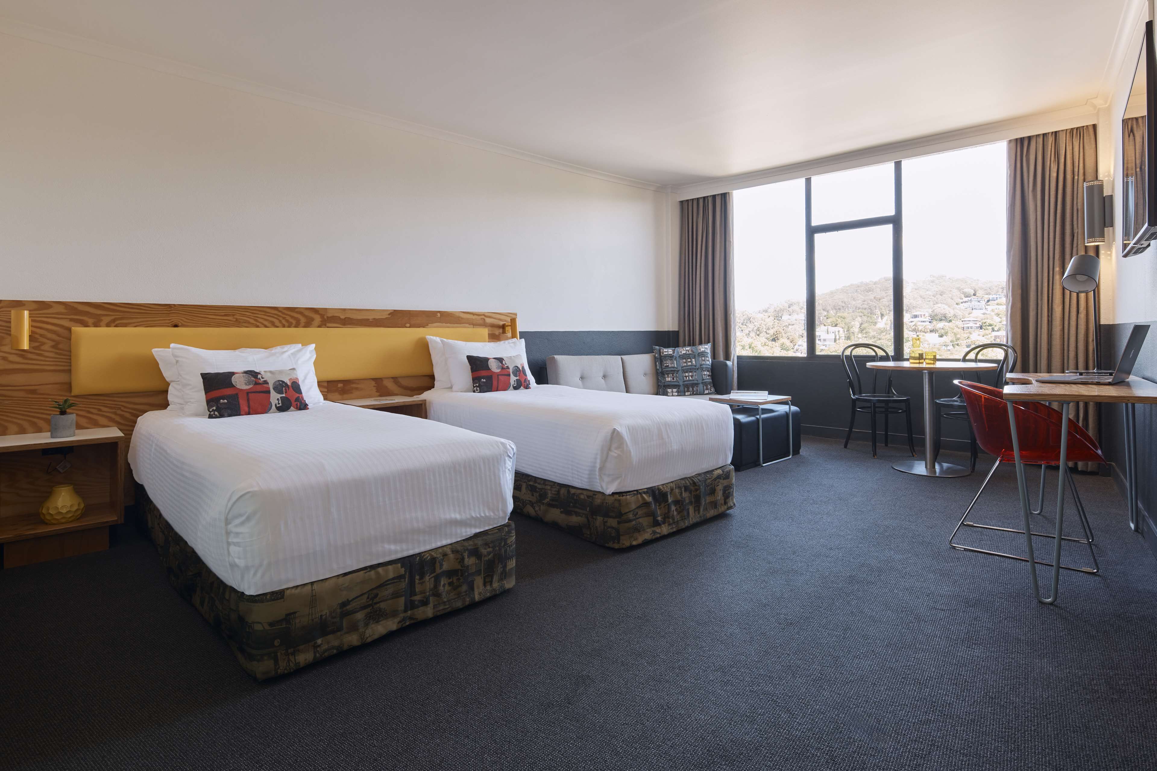 A hotel room with two beds, a desk, a chair, and a view of the city.