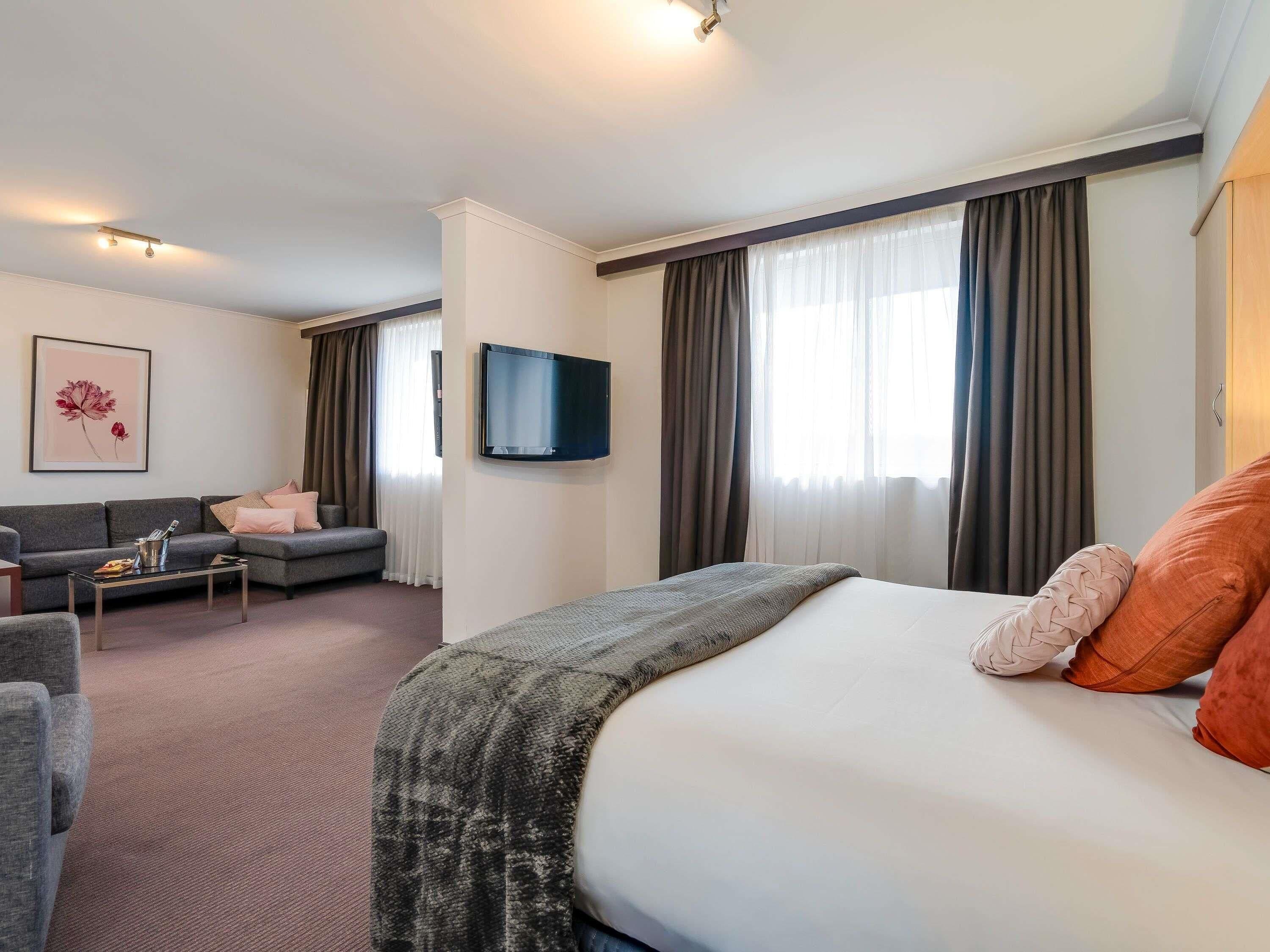 A hotel room with a bed, a sofa, a TV, and a painting on the wall.