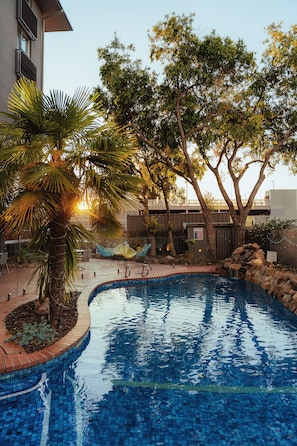 A swimming pool with tiled edges, surrounded by palm trees and a brick walkway. - Mercure Albury (Albury)