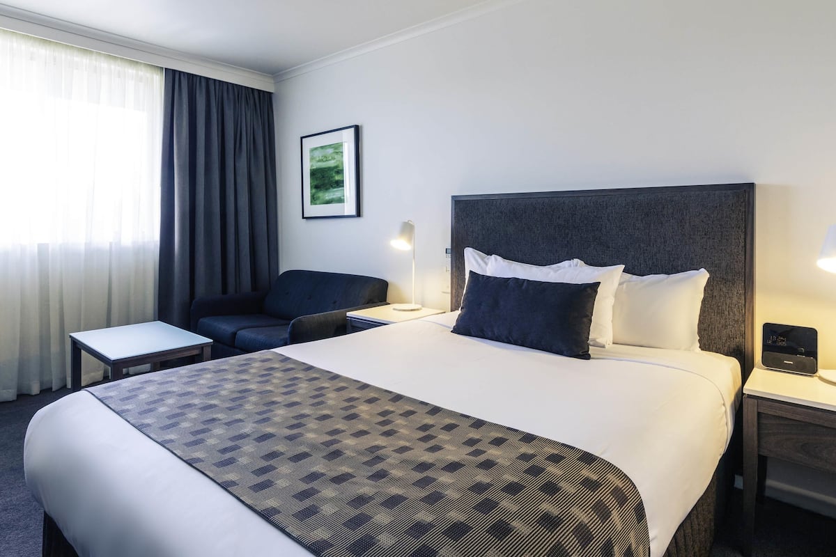 Habitación de hotel con cama, mesitas de noche, escritorio, silla, lámpara y un cuadro en la pared.