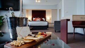 Une chambre d’hôtel équipée d’un lit, d’une table de chevet, d’un bureau, d’une télévision et d’un plateau de petit-déjeuner avec de la nourriture et une bouteille de champagne.
