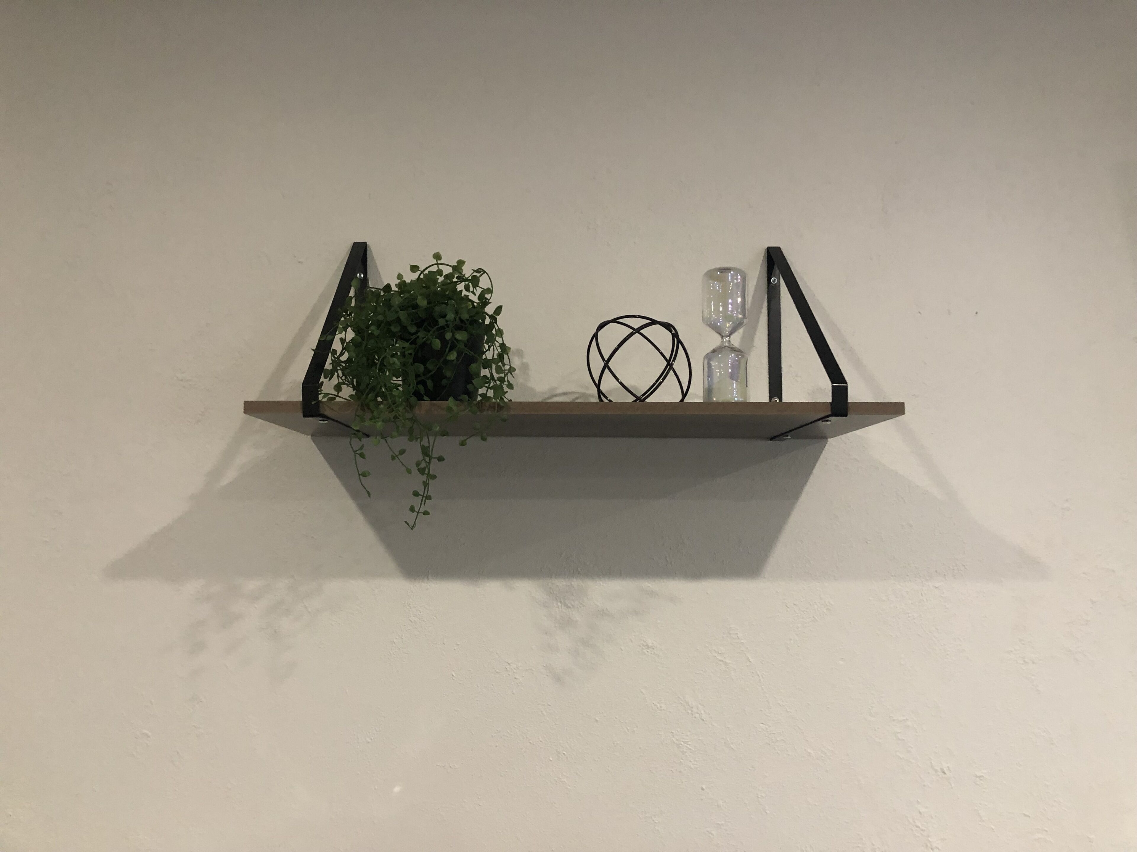Een houten plank met een potplant, twee zandlopers en een opgerolde draadsculptuur, geplaatst tegen een effen muur.